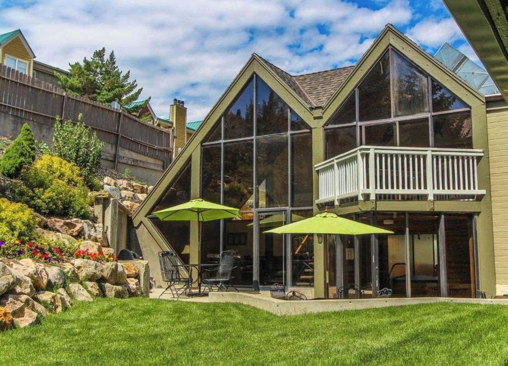 A residential building with a balcony, large windows, and outdoor seating with umbrellas.