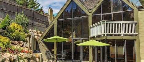 A residential building with a balcony, large windows, and outdoor seating with umbrellas.