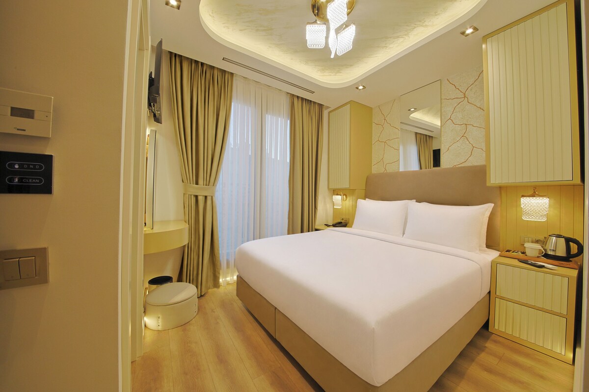 A hotel room with a large bed, bedside tables, a wardrobe, a bathroom with a toilet, and a ceiling light fixture.