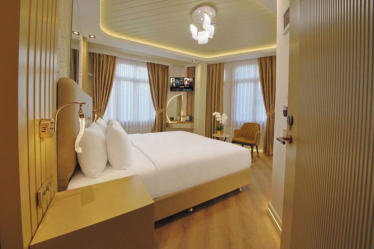 A hotel room with a large bed, a bedside table, a TV, a mirror, and a door.