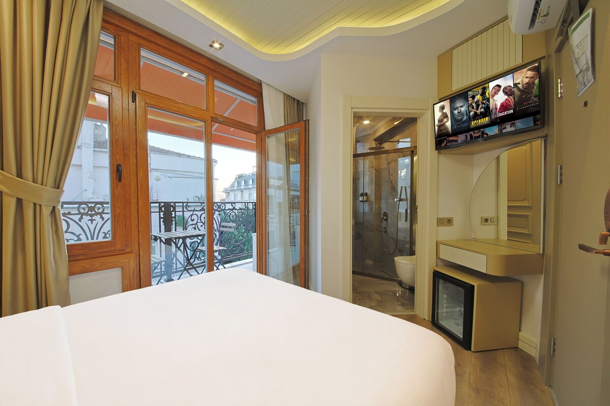A hotel room with a large bed, a TV mounted on the wall, and a balcony with a view of the city.