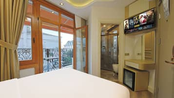 Habitación de hotel con una cama grande, un televisor montado en la pared y un balcón con vistas a la ciudad.