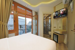 A hotel room with a large bed, a TV mounted on the wall, and a balcony with a view of the city. - Colombo Hotel (İstanbul)