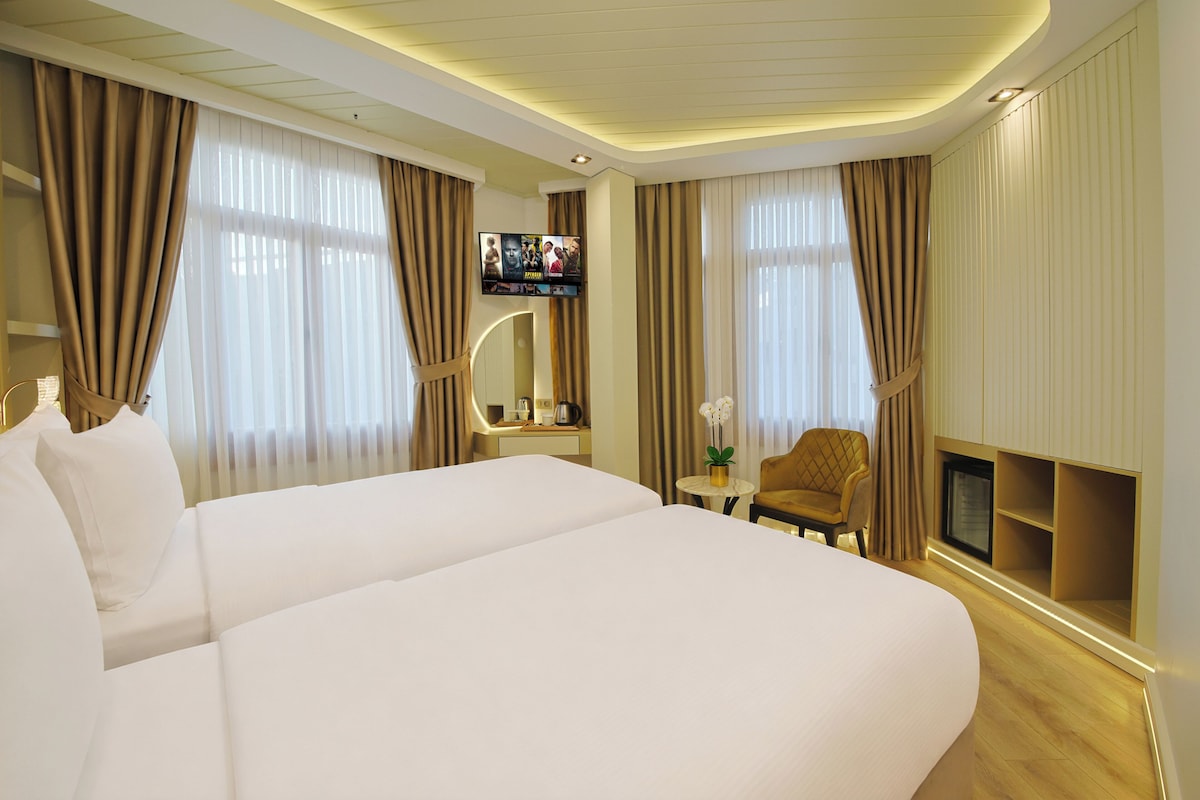 A hotel room with a large bed, a TV, a small table with a vase of flowers, and a fireplace.