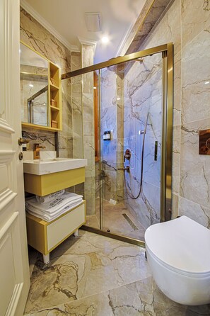 A bathroom with a glass-enclosed shower, marble flooring, a white toilet, and a vanity with a mirror. - Colombo Hotel (İstanbul)