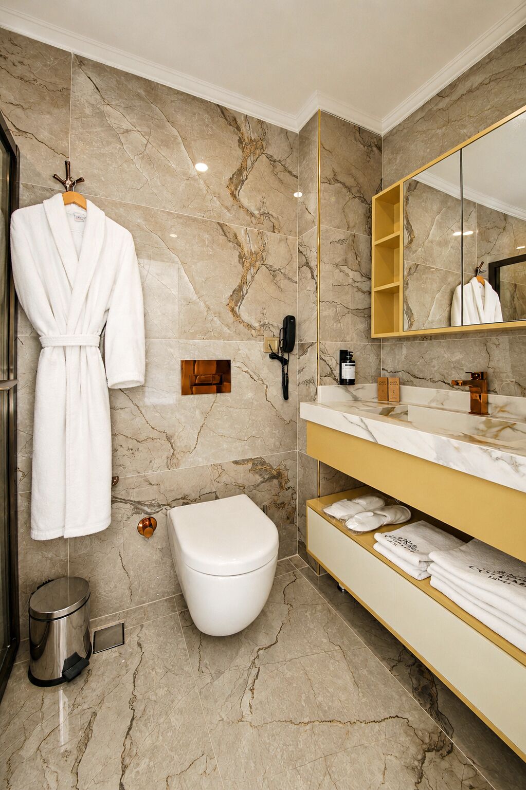 Un baño moderno con piso de mármol, inodoro blanco, tocador con espejo y una bata colgada en un perchero.