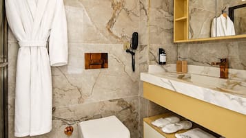 Un baño moderno con piso de mármol, inodoro blanco, tocador con espejo y una bata colgada en un perchero.