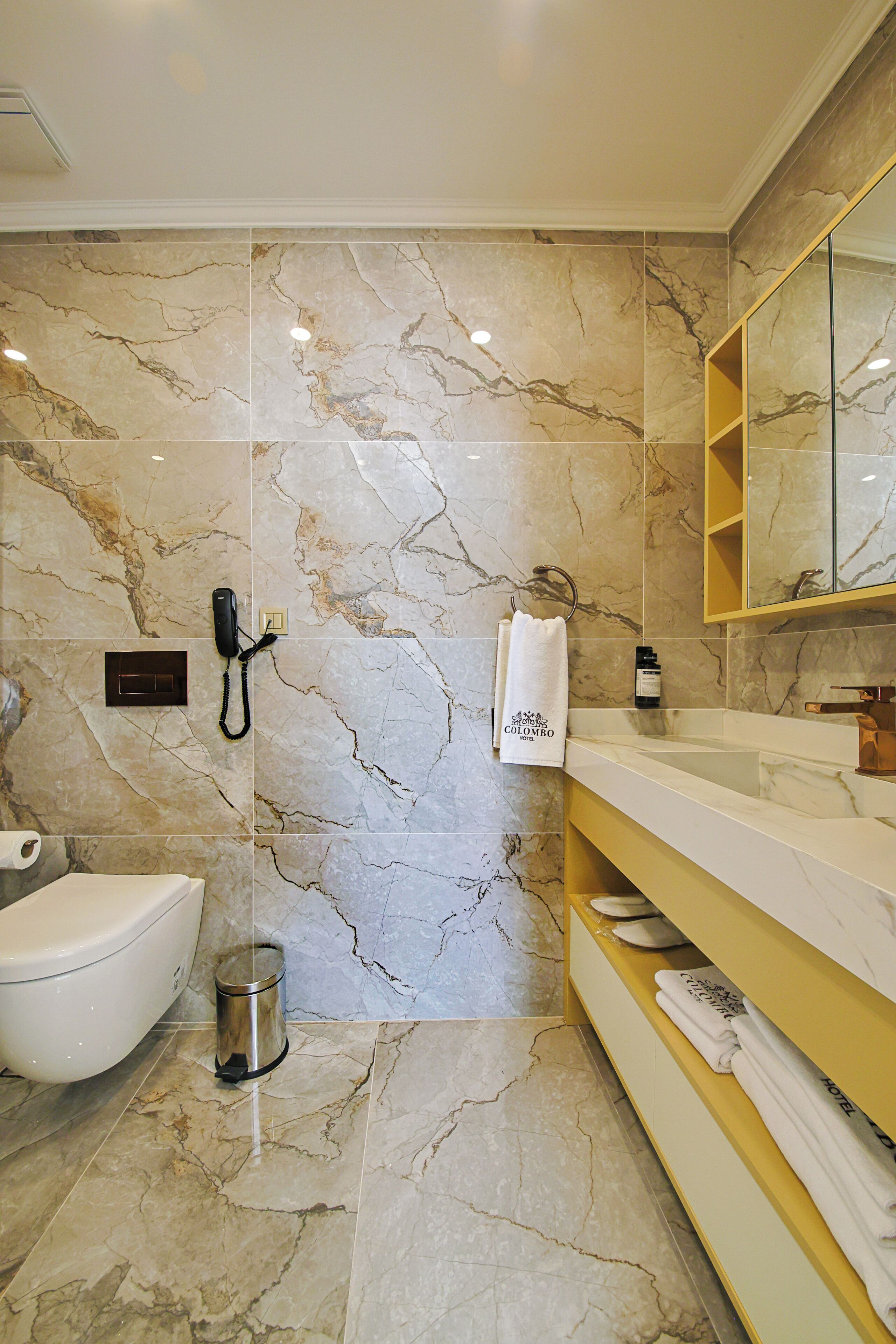 A modern bathroom with a marble wall, a toilet, a sink with a mirror, and a towel rack.