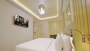 Habitación de hotel con cama, mesita de noche, teléfono, espejo y televisor de pared mostrando carteles de películas.