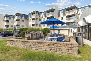 Un edificio residencial de varios pisos con balcones, mobiliario exterior y un muro de contención de piedra.