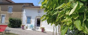 A courtyard with a white building, a red chair, and potted plants. - A QUIET COUNTRY COTTAGE FOR VACATION, BUSINESS TRIPS, OR SPA TREATMENTS (Salignac-de-Mirambeau)