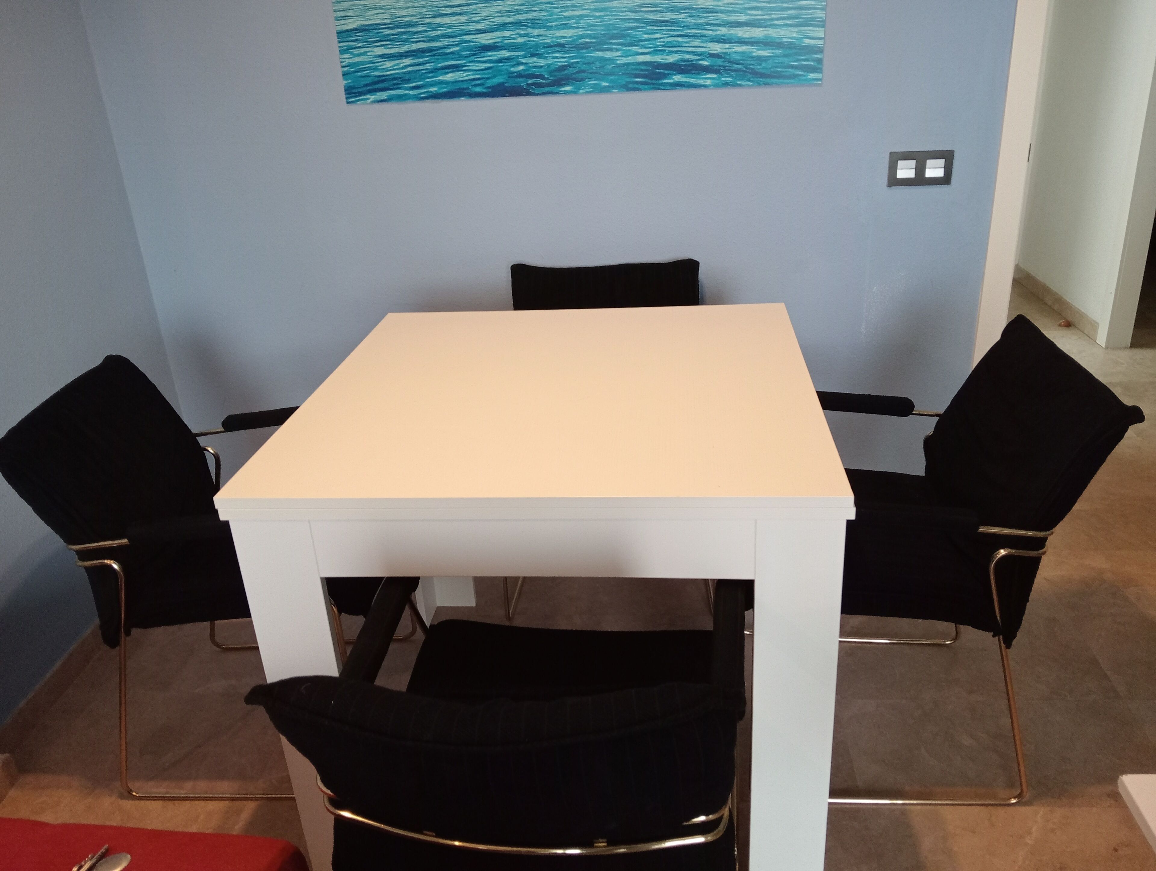 Une pièce avec une table blanche et quatre chaises noires.
