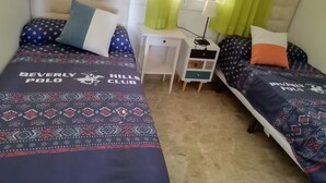 Una camera da letto con due letti, ognuno con una coperta e dei cuscini a motivi, un comodino con una lampada, e una finestra con tende.