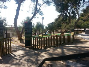 Ein Spielplatz mit umzäunter Fläche, Bäumen und einem Hinweisschild.