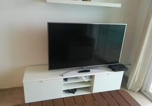 Televisão de tela plana em um móvel branco com controle remoto e um dispositivo preto em cima.