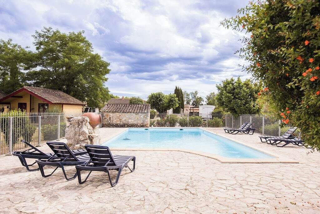 Une piscine avec des chaises longues, une terrasse en pierre et un espace clos avec des arbres et un bâtiment en arrière-plan.