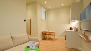 Ein kompakter Wohnraum mit Sofa, Esstisch mit Stühlen, einer kleinen Küchenzeile und einem Fernseher.