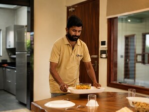 A person serving food at a table in a modern kitchen with a dining area.
