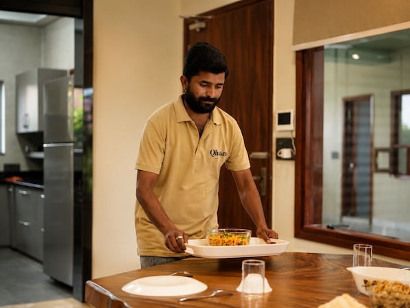 A person serving food at a table in a modern kitchen with a dining area.