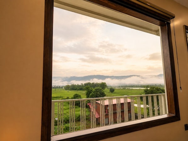 A window with a view of a green landscape, a white railing, and a building with a red roof.