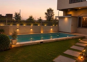 A rectangular swimming pool with a tiled edge, surrounded by a well-maintained lawn and a low fence.