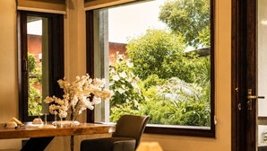 A room with a dining table, chairs, a lamp, and a view of greenery outside.