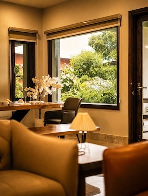 A room with a dining table, chairs, a lamp, and a view of greenery outside.