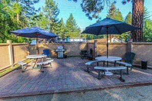 Una terrazza esterna con tavoli da picnic e ombrelloni, circondata da un muro in mattoni e alberi.