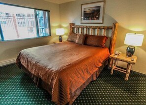 Una camera d'hotel con un letto grande, due lampade sui comodini, un tavolino con lampada, una finestra con tende e un quadro appeso al muro.
