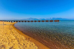 Una spiaggia con acque limpide, una riva sabbiosa e moli in legno che si protendono nel mare.