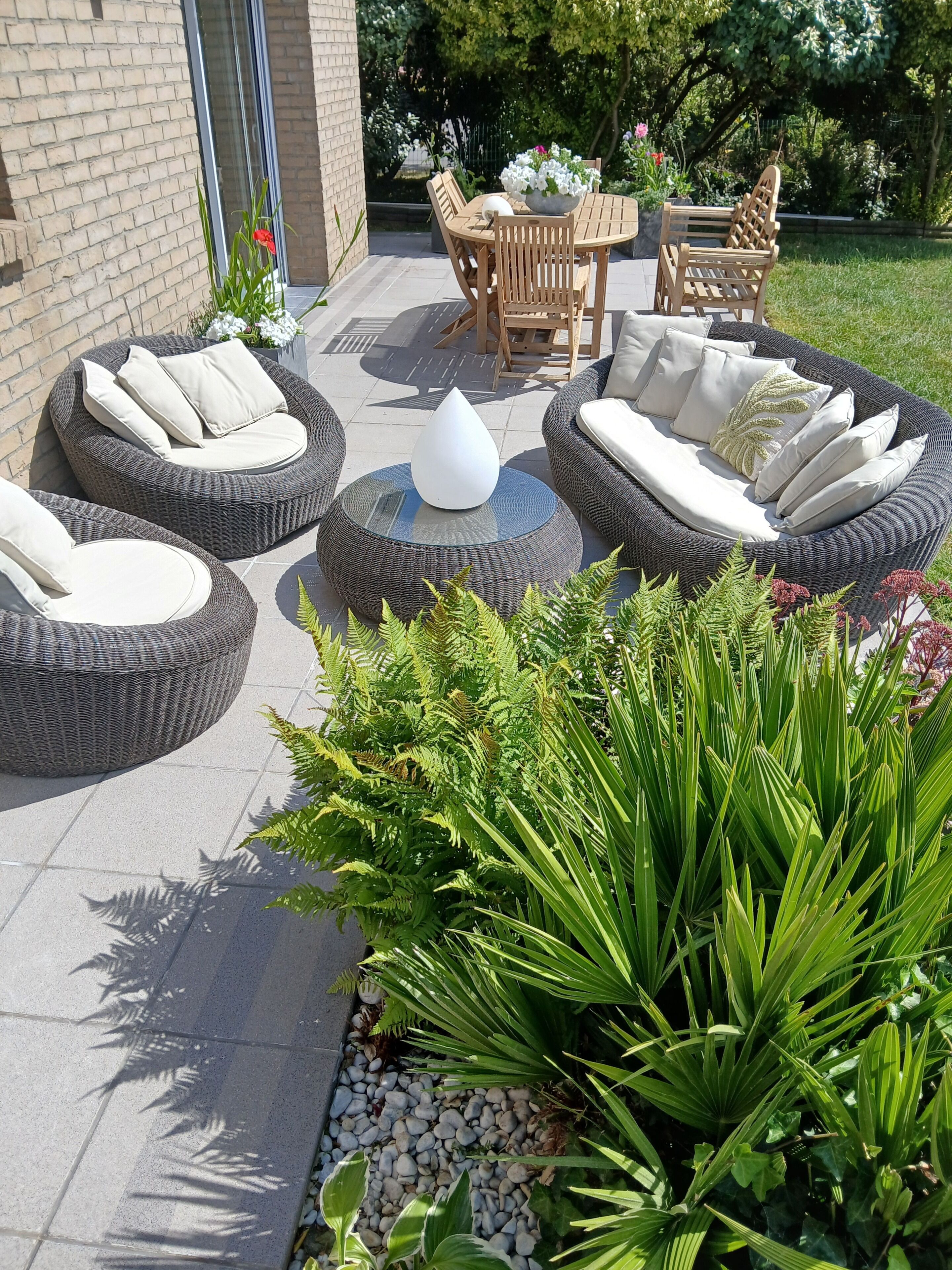 Espace extérieur aménagé avec des tables et des chaises rondes, entouré de verdure et d’un mur de briques.