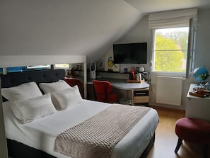 A bedroom with a bed, a desk, a chair, a television, and a window with a view of trees. - Welcome to a haven of tranquility in Zuydcoote (Zuydcoote)