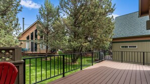 A wooden deck with a metal railing, a red chair, and a house with a chimney in the background.