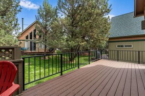 A wooden deck with a metal railing, a red chair, and a house with a chimney in the background.