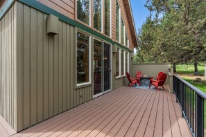 Une terrasse avec un foyer en pierre et des chaises rouges, entourée d’une autre terrasse en bois et d’une clôture verte.