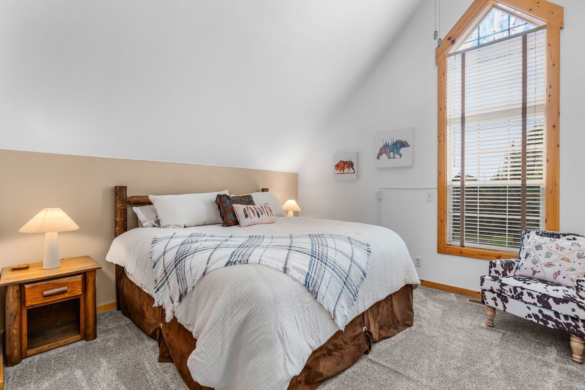 A bedroom with a bed, bedside tables, a chair, and a window with blinds.