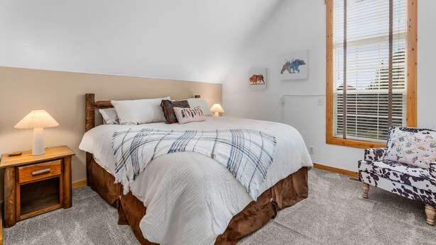 A bedroom with a bed, bedside tables, a chair, and a window with blinds.