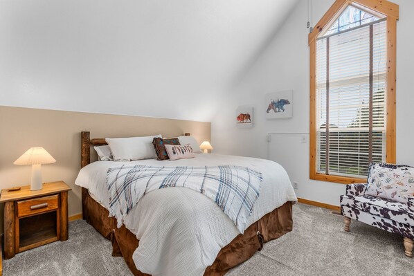 A bedroom with a bed, bedside tables, a chair, and a window with blinds.