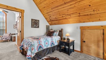 A bedroom with a sloped ceiling, a bed with a patterned bedspread, a nightstand with a lamp, and a door.