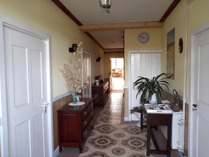 A hallway with a tiled floor, wooden furniture, a clock on the wall, and a door at the end.