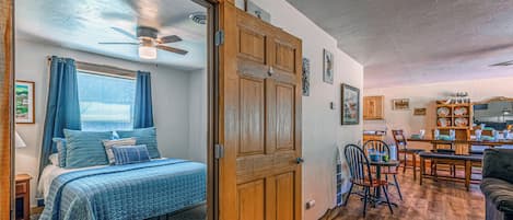 Un dormitorio con una cama, un ventilador de techo y vista al área de comedor contigua.