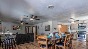 A spacious living area with a dining table, chairs, a sofa, and a ceiling fan.