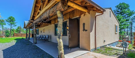 A rustic cabin with a wooden porch, outdoor seating, and a door with a metal handle.