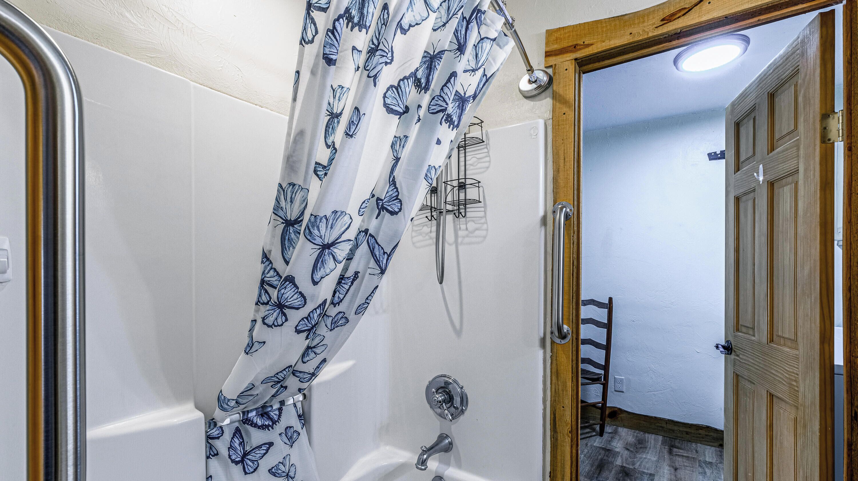 A bathroom with a shower curtain featuring a butterfly pattern, a handheld showerhead, and a wooden door leading to a hallway.