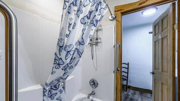 A bathroom with a shower curtain featuring a butterfly pattern, a handheld showerhead, and a wooden door leading to a hallway.