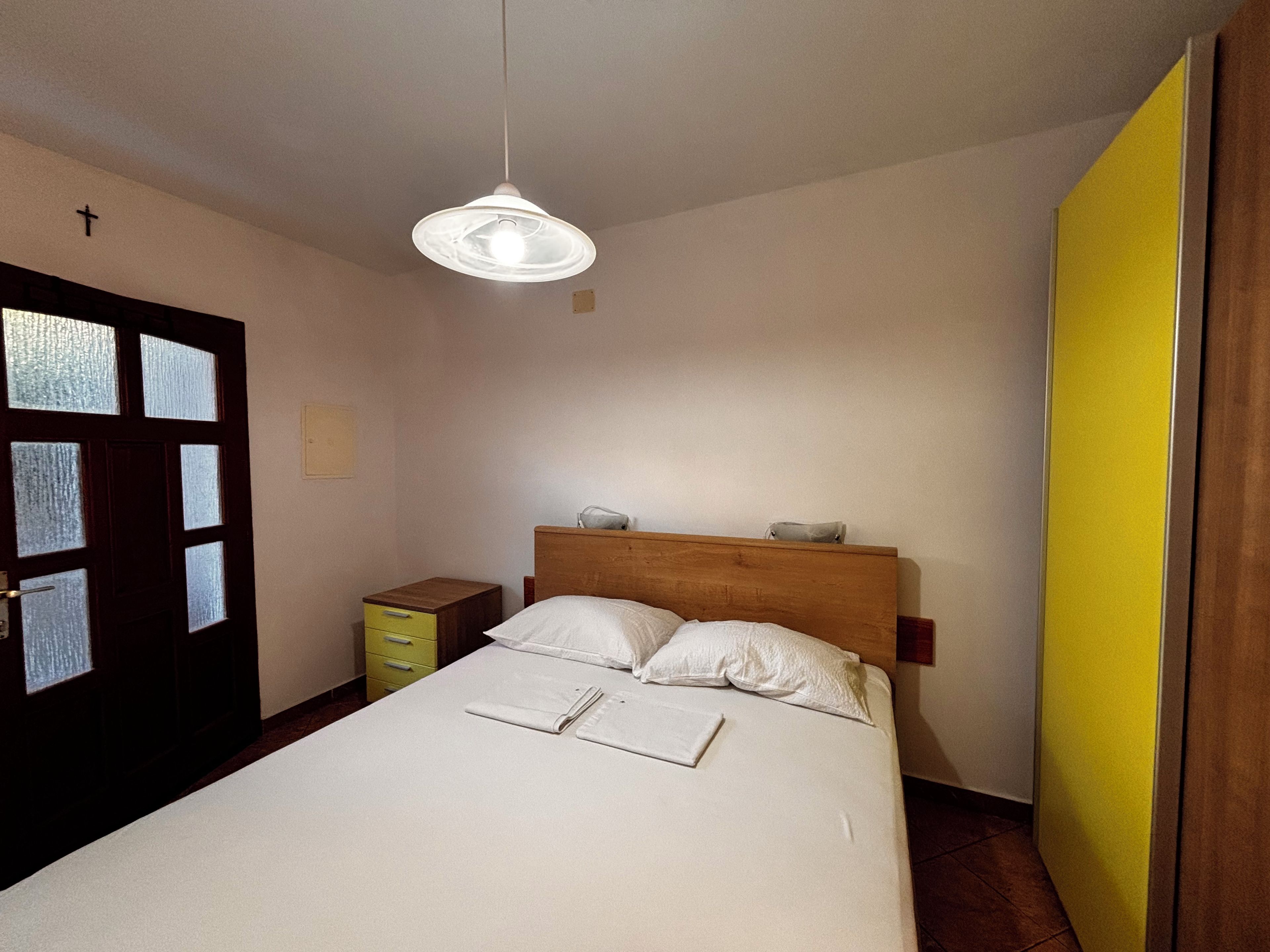 A bedroom with a bed, a bedside table, a nightstand, and a hanging light fixture.