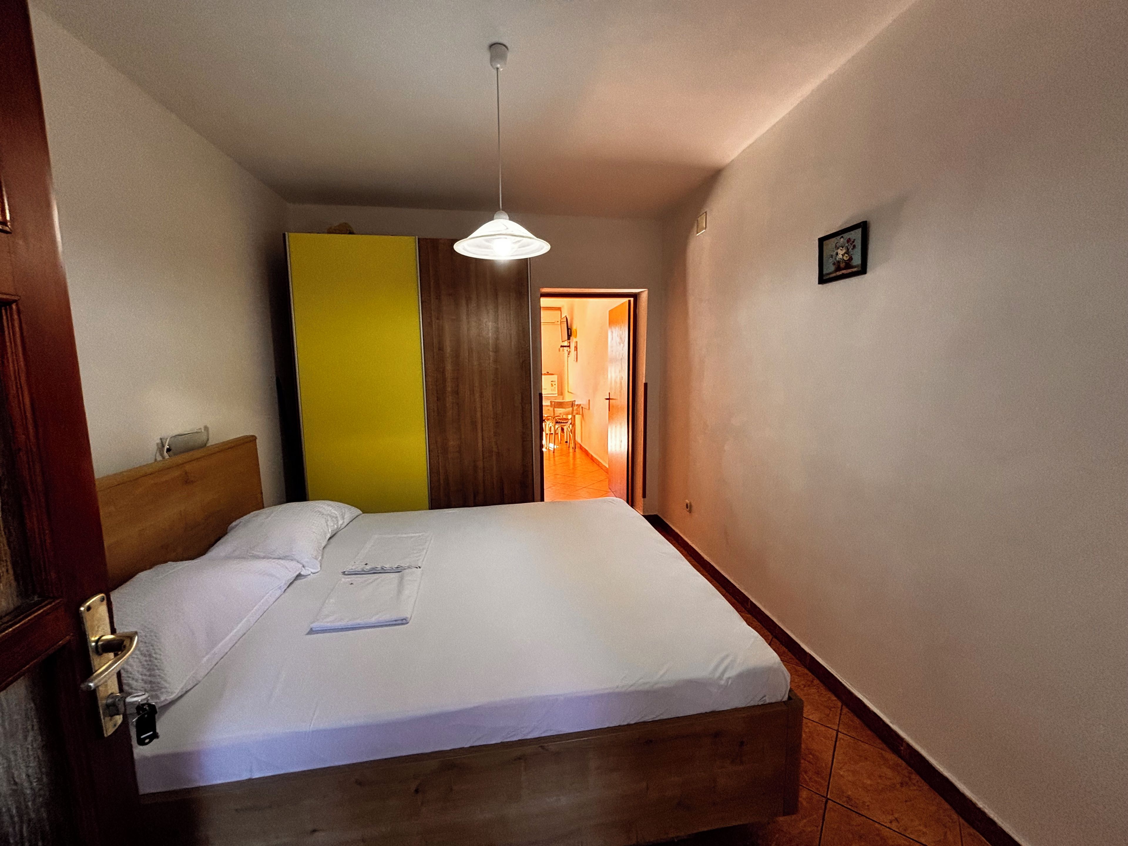 Habitación de hotel con cama, cabecera de madera, lámpara colgante y puerta que da a un pasillo.