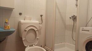 Un bagno con il water, una cabina doccia e una lavatrice.