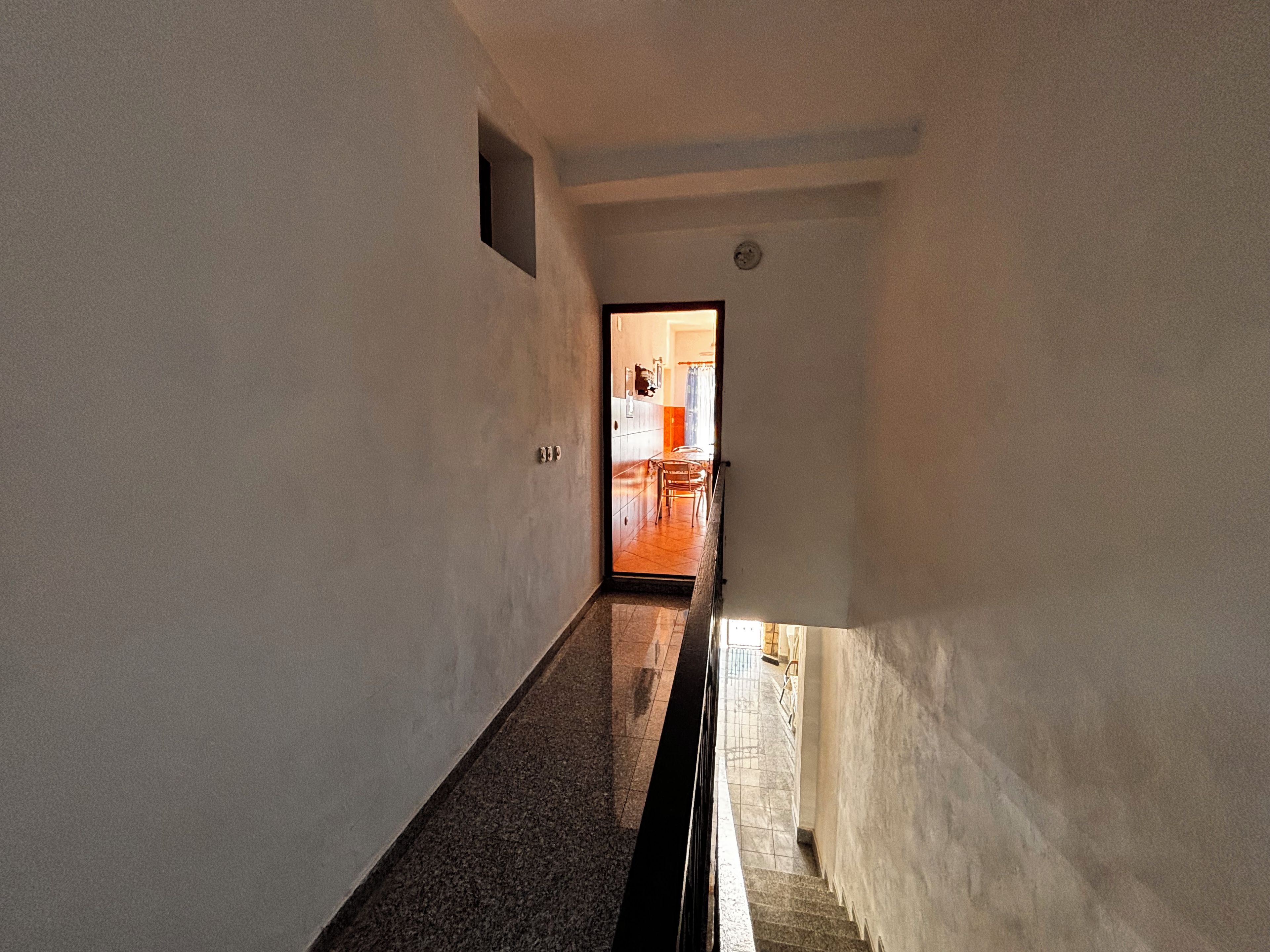 A narrow hallway with a door leading to a room with a tiled floor and a visible chair.
