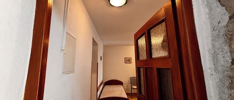 A hallway leading to a bedroom with a bed, a door with a number plate, and a light fixture on the ceiling.
